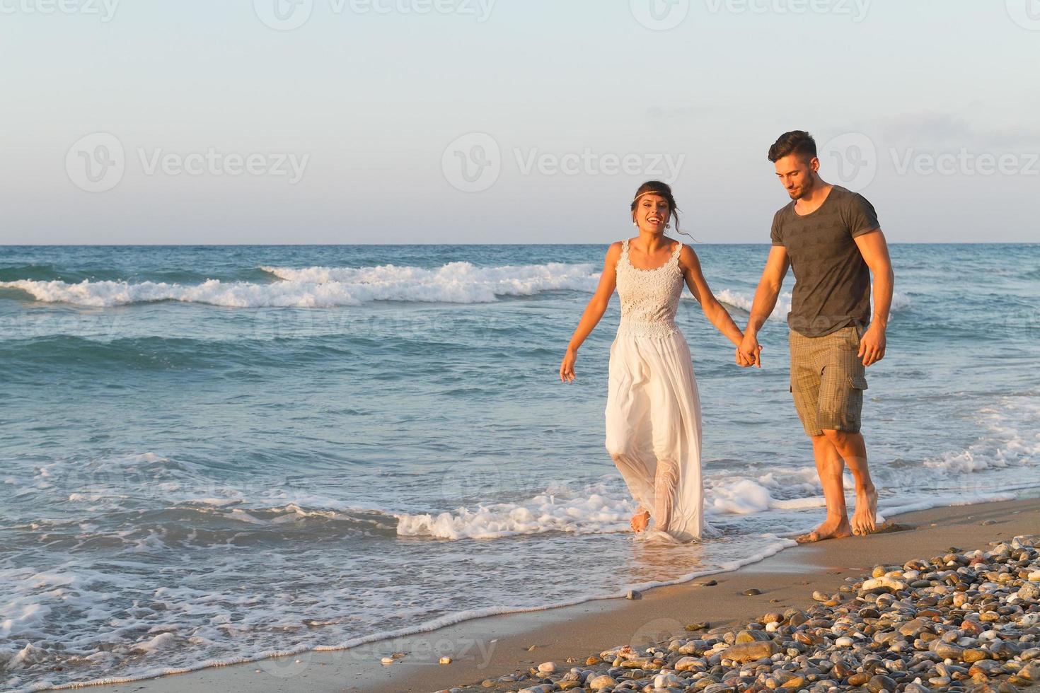 unga par tycker om att gå på en disig strand i skymningen foto