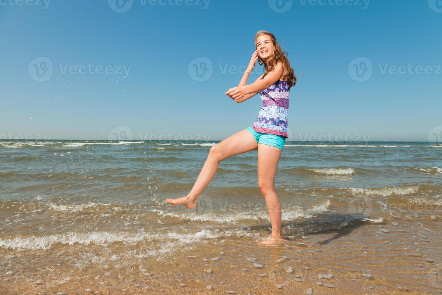 glad tjej med långt brunt hår njuter av den uppfriskande stranden. foto