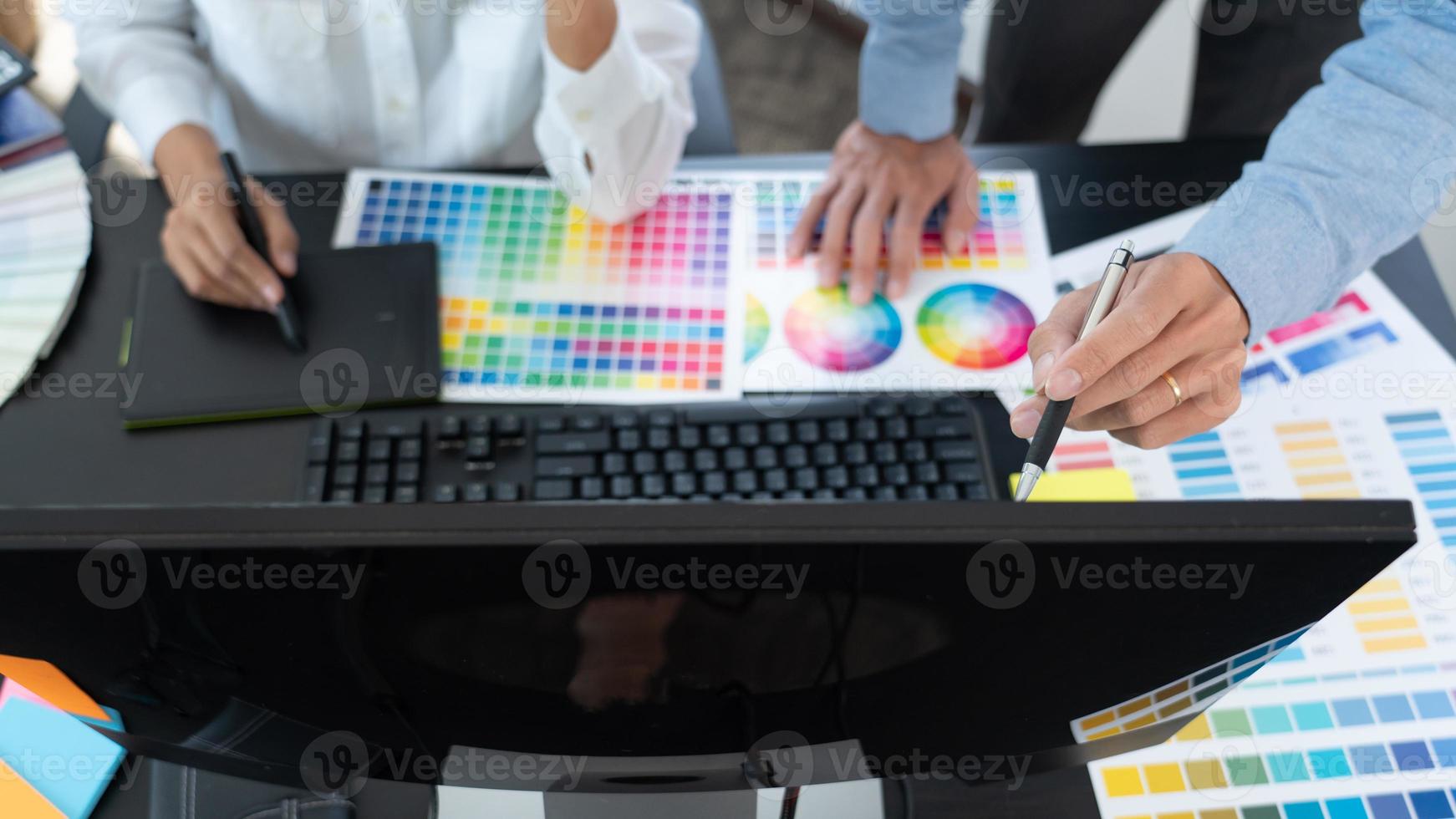 grafisk designerteam som arbetar med webbdesign med färgprover som redigerar konstverk med surfplatta och en penna vid skrivbord på kreativa kontor foto