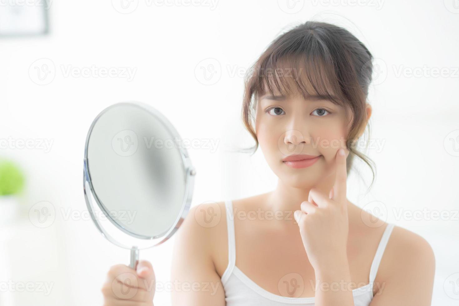 vacker ung asiatisk kvinna som tittar i spegeln med akneproblem i sovrummet, besvär med skönhet i ansiktet, zitbehandling, asiatisk flicka är finne med oro och missnöje, hudvård och hälsosamt koncept. foto