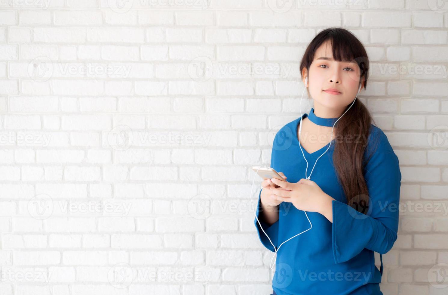 vackert porträtt asiatisk ung kvinna står glad njuta och roligt lyssna musik med hörlurar på cement betong bakgrund, livsstil av flicka slappna av ljud radio med hörlurar, teknik koncept. foto