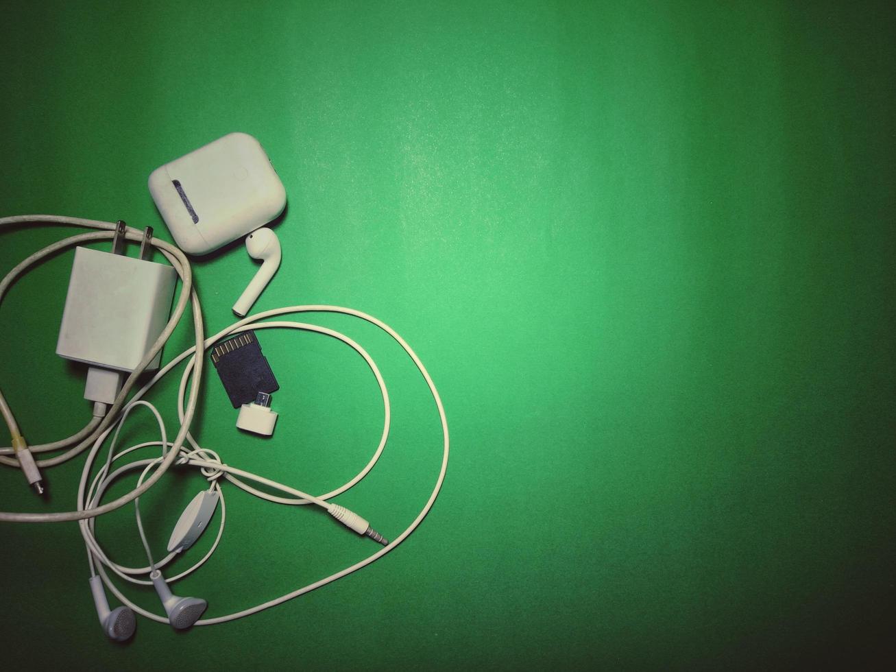 telefonladdare och vita hörlurar placerade på en grön bakgrund med vinjetter, vintage stil, kopieringsutrymme. foto