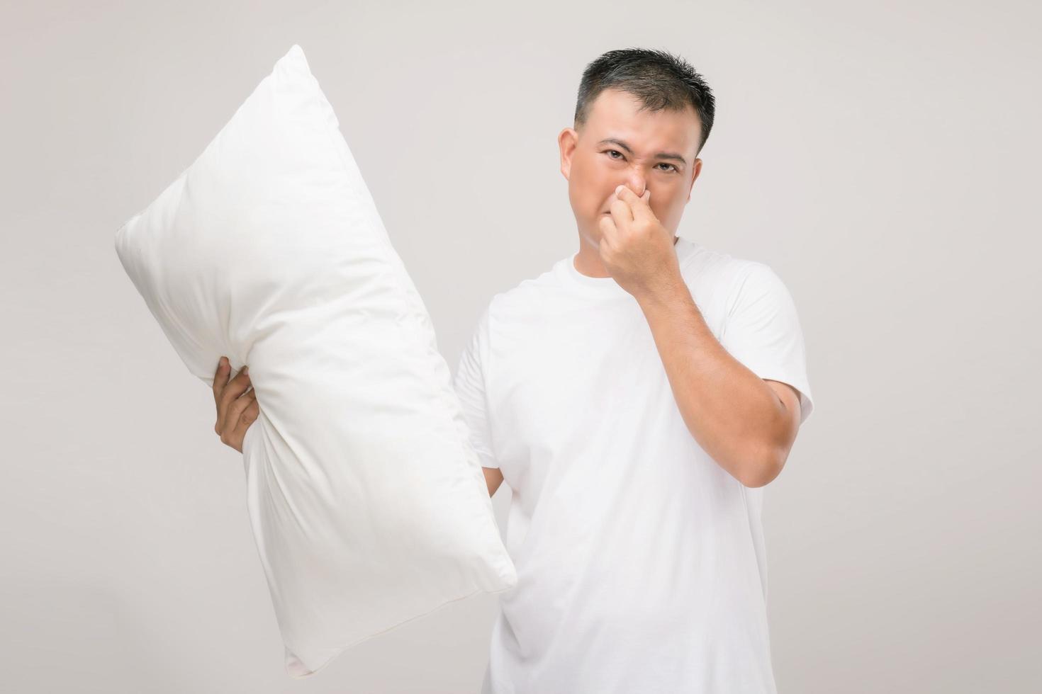 kudden luktar illa. porträtt asiatisk man som håller vit kudde och får dålig lukt. studio skott på grått foto