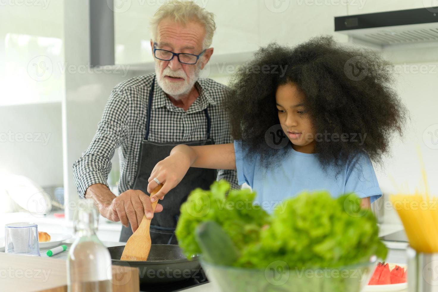 familjesemesteraktiviteter med farfar och barnbarn. lagar middag tillsammans för familjen farfar lär ut matlagning till sitt halvasiatiska barnbarn afroamerikaner foto
