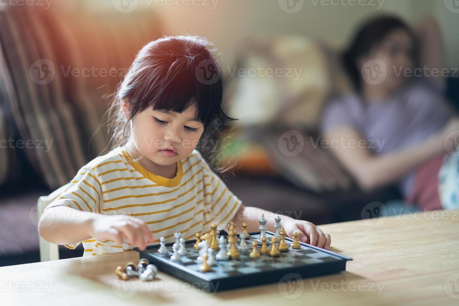 liten asiatisk baby som spelar schack i vardagsrummet hemma. smart kid. mode barn. litet genibarn. intelligent spel.schackbräde. baby aktivitet koncept. foto