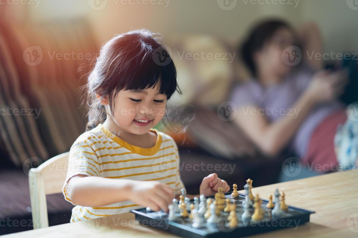 liten asiatisk baby som spelar schack i vardagsrummet hemma. smart kid. mode barn. litet genibarn. intelligent spel.schackbräde. baby aktivitet koncept. foto