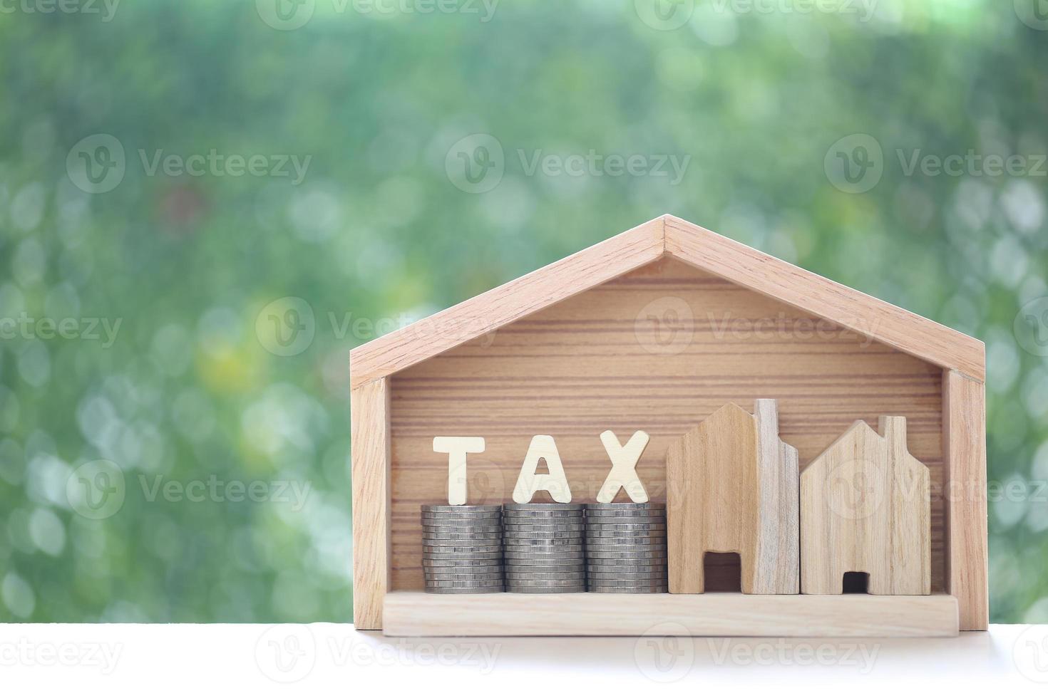fastighetsskatt, modellhus med bunt med myntpengar och skatteord på grön bakgrund, affärsinvestering och fastighetsskattekoncept foto