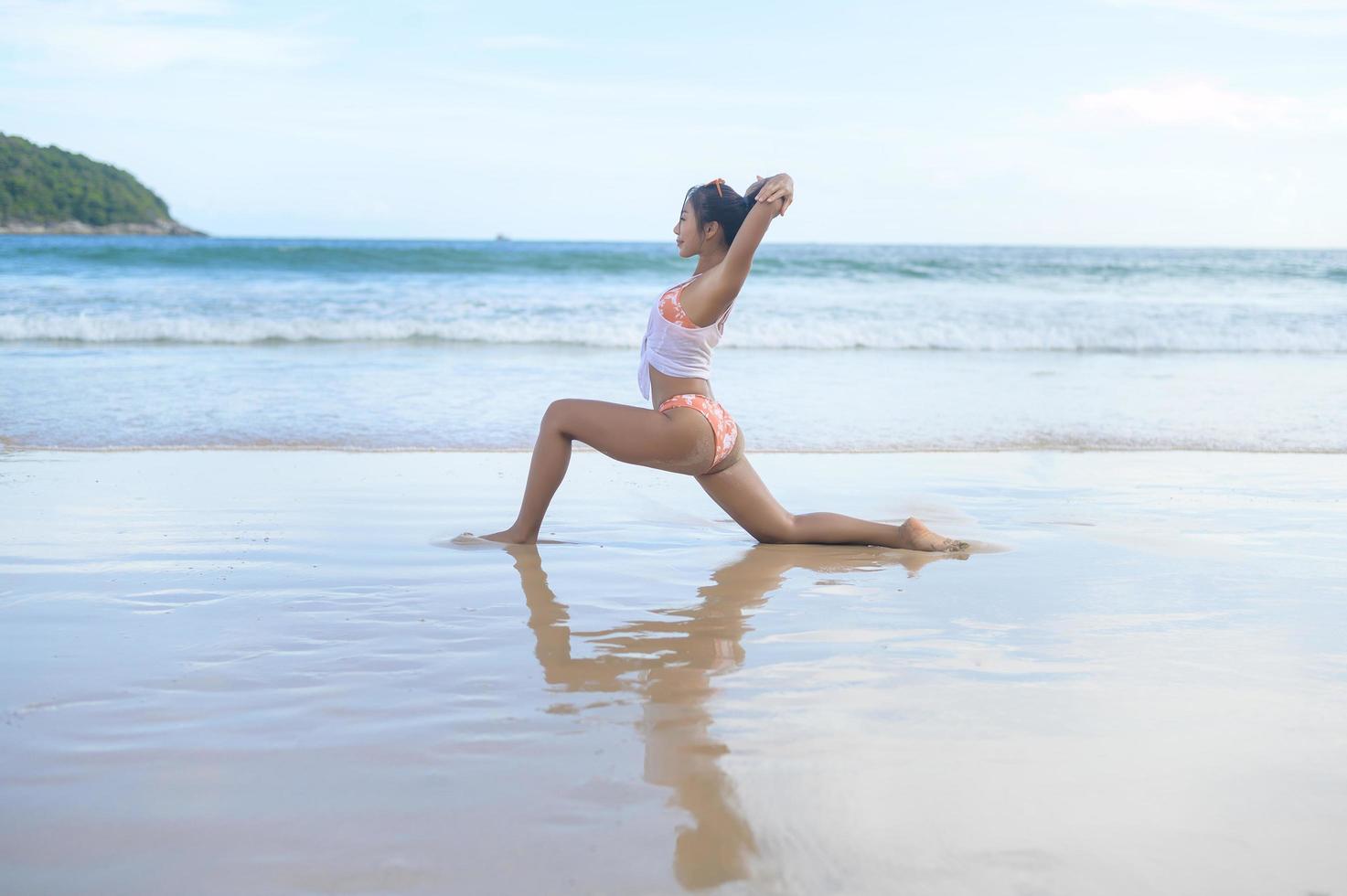 ung asiatisk kvinna i bikini gör yoga på stranden, hälsa och meditation koncept foto