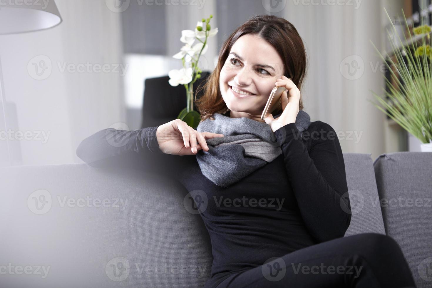 brunettkvinna som sitter på soffan och pratar i telefon foto