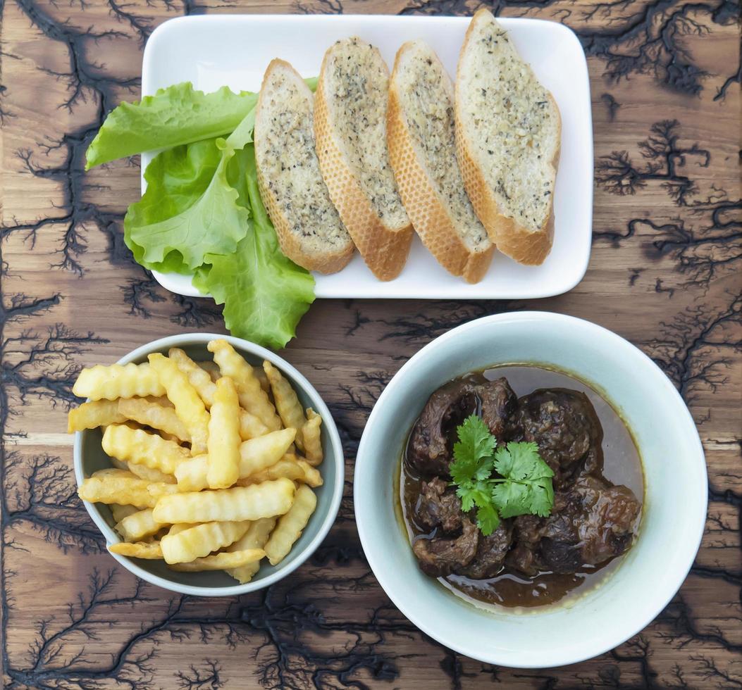 oxgryta servera med pommes frites och vitlöksbröd foto