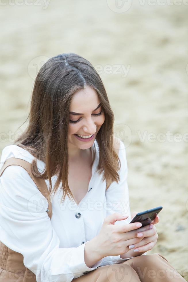 flicka utomhus textar på sin mobiltelefon. flicka med telefon. porträtt av en glad kvinna text sms på hennes telefon. foto