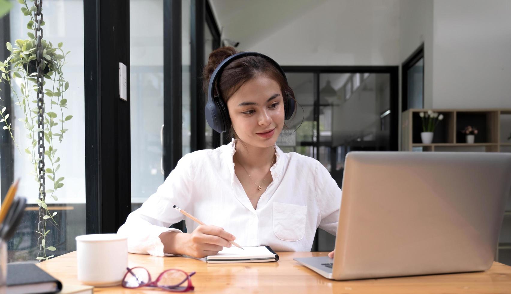 asiatisk kvinna tolk skriva översättning från främmande språk till engelska lyssna på ljudinspelning i headset. foto