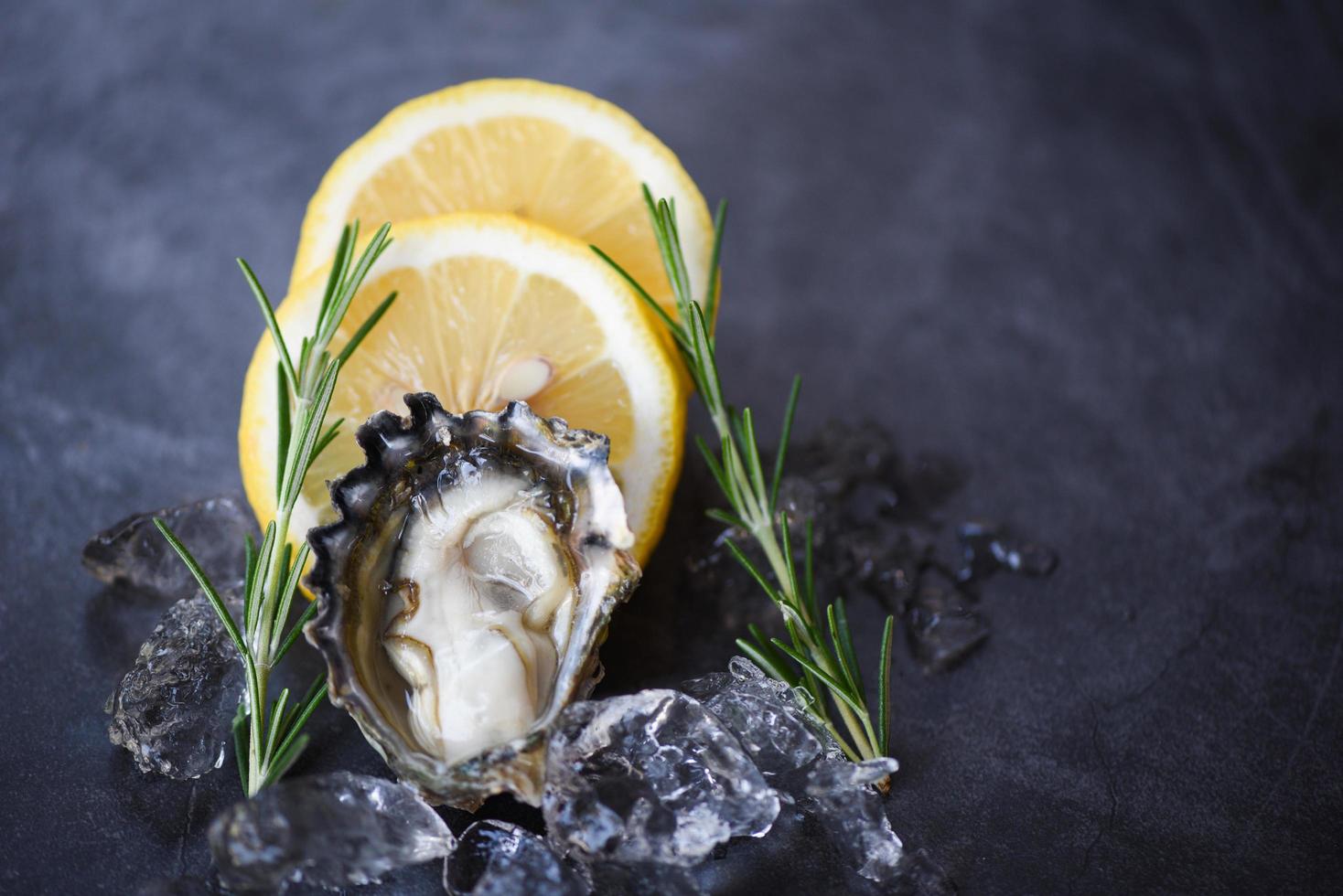 närbild öppet ostronskal med örtkryddor citron rosmarin serveras bord och is hälsosam skaldjur rå ostron middag i restaurangen gourmetmat färsk ostron skaldjur på svart tallrik bakgrund foto