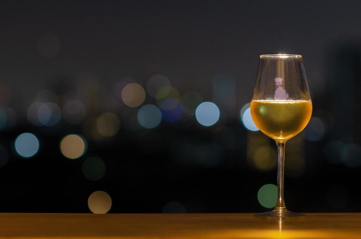 ett glas vitt vin på träbordet i takbaren med färgglad bokeh av stadsljus och utrymme för text. foto