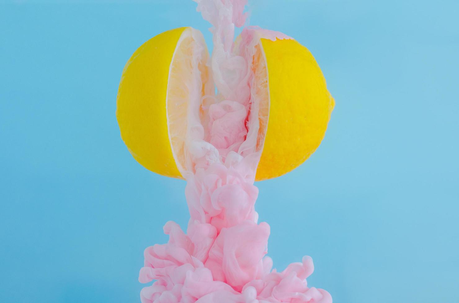 partiell fokus på att lösa upp rosa affischfärg i vattendroppe mellan två skivor citroner på blå bakgrund foto