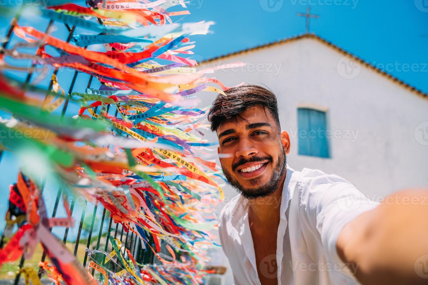 leende vänlig ung latinamerikansk man som tar en selfie med de färgglada banden från vår herre av bonfim. foto