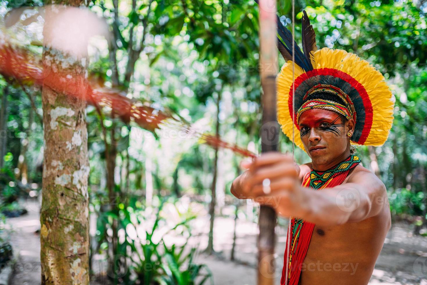 indian från pataxo-stammen med hjälp av pil och båge. brasiliansk indian med fjäderhuvudbonad och halsband foto