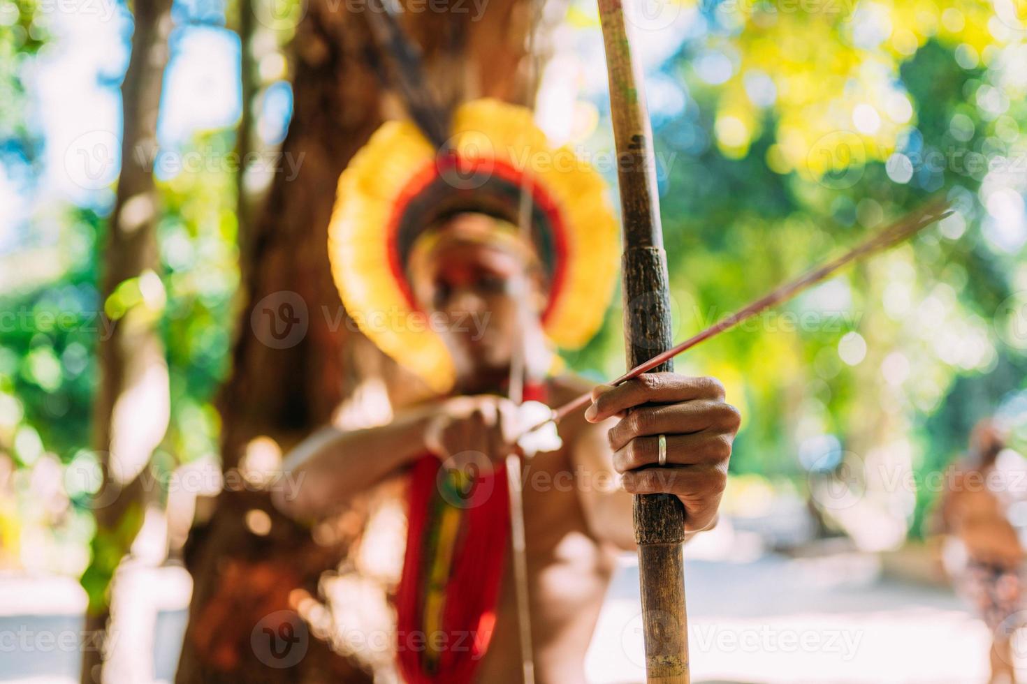 indian från pataxo-stammen med hjälp av pil och båge. brasiliansk indian med fjäderhuvudbonad och halsband. fokusera på pil och båge foto