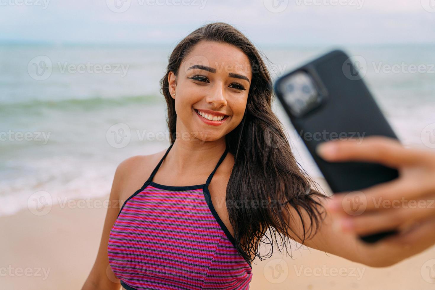 vacker latinamerikansk kvinna som gör selfiestrandbakgrund, soliga sommarfärger. foto