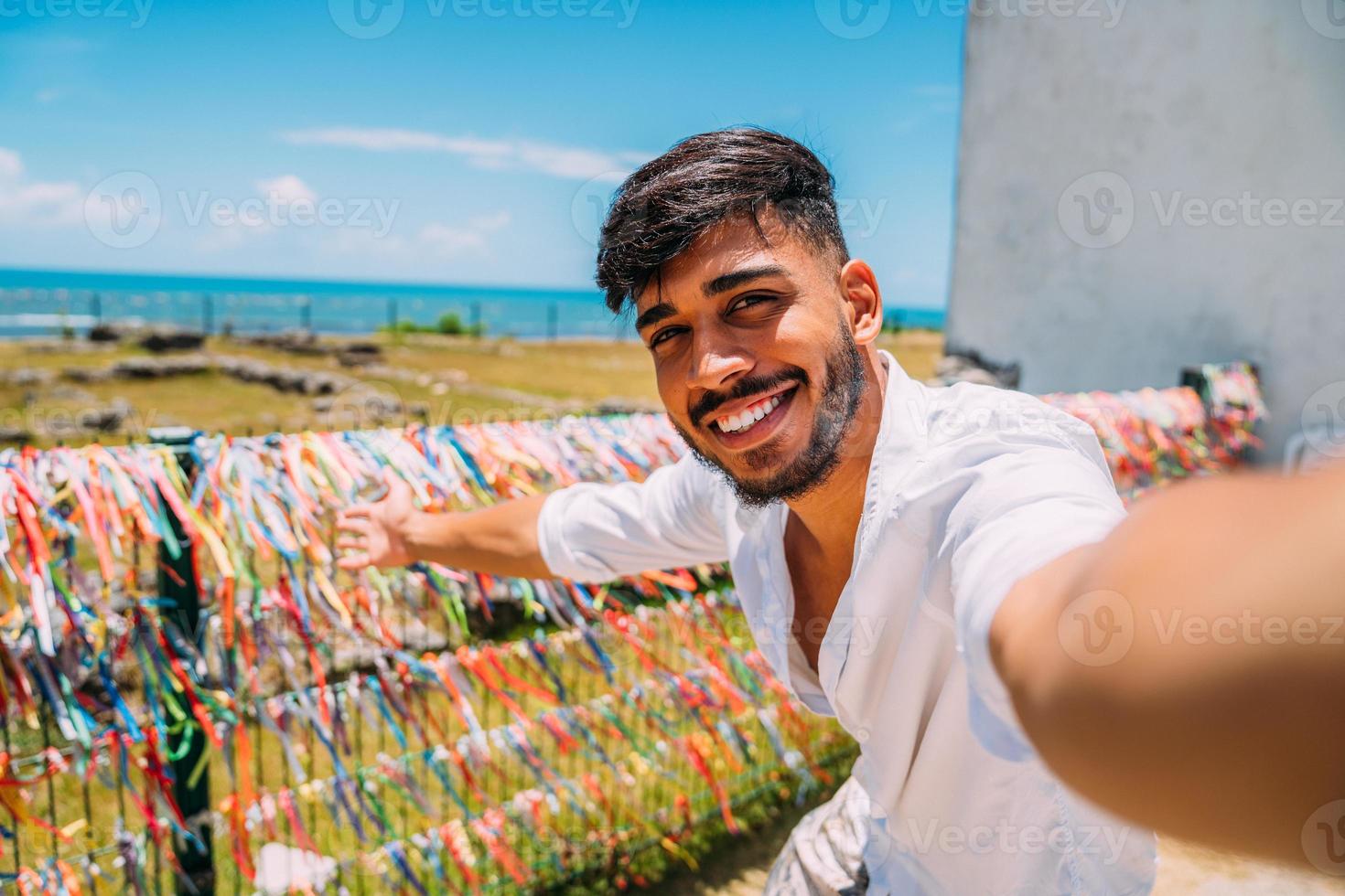 vänlig ung latinamerikansk man som bjuder in att komma till Brasilien, självsäker och ler gör en gest med handen, är positiv och vänlig foto