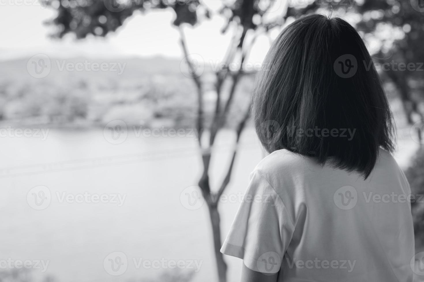 bakifrån av ledsen asiatisk kvinna i parken ser utsikten över sjön. deprimerad kvinna. mental hälsa koncept. oro och ångest kvinna. olyckligt liv. ensam och ensam person. svartvit fotografering. foto