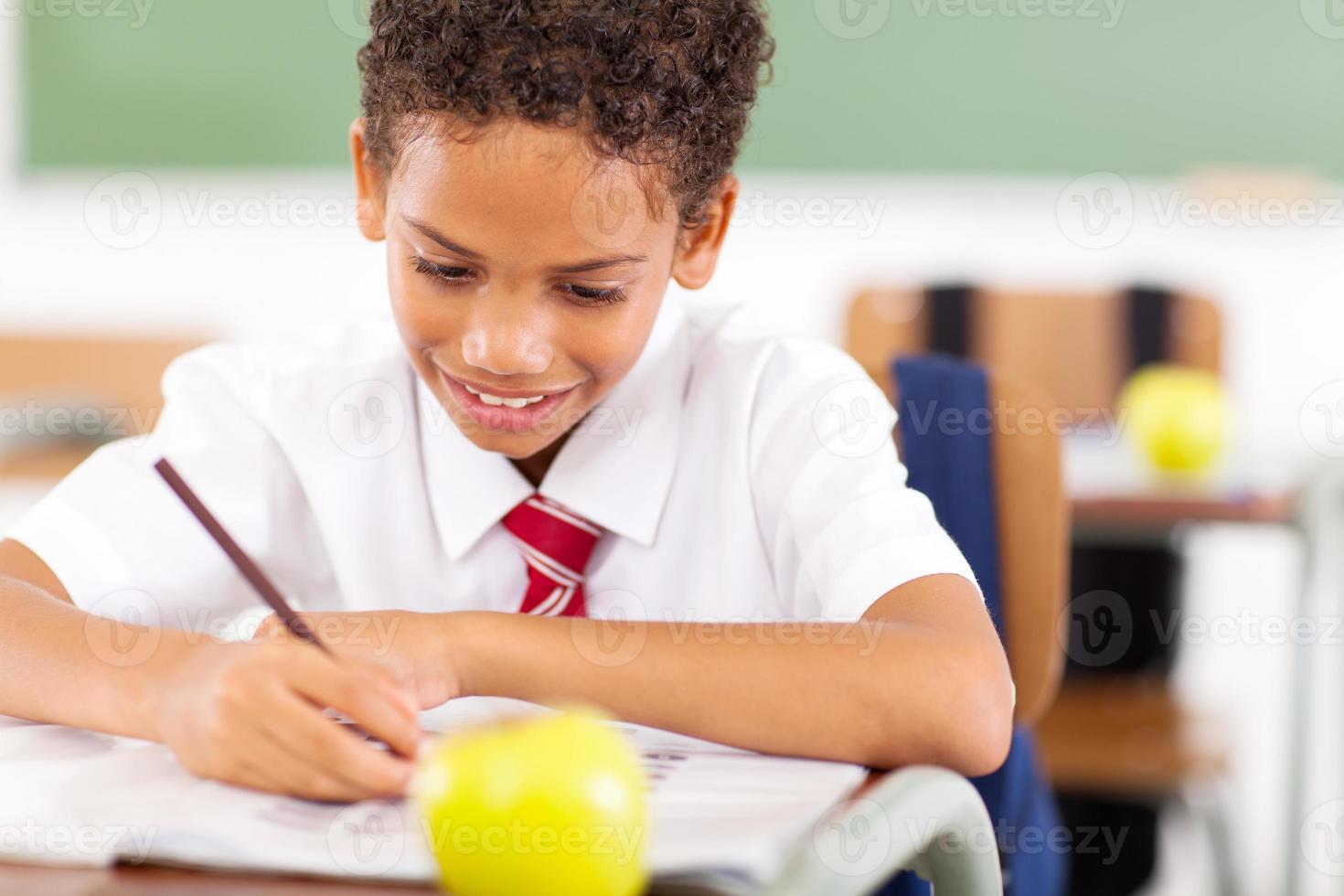 grundskolepojke som skriver klassarbete foto
