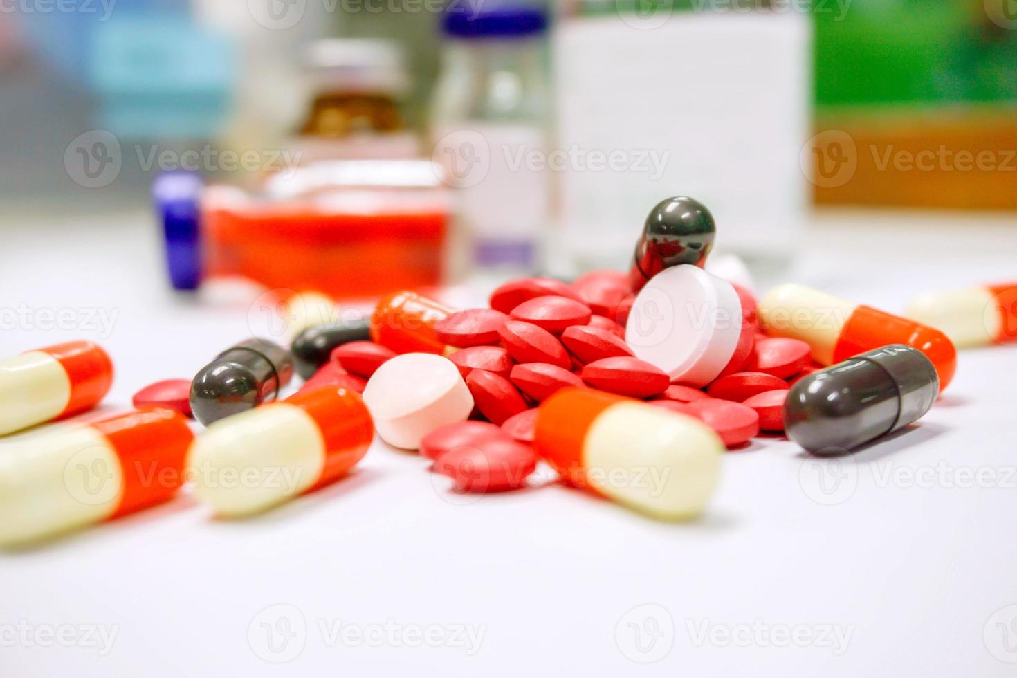 närbild av röda piller mediciner och kapsel plats på vitt bord med ampul suddig bakgrund. foto