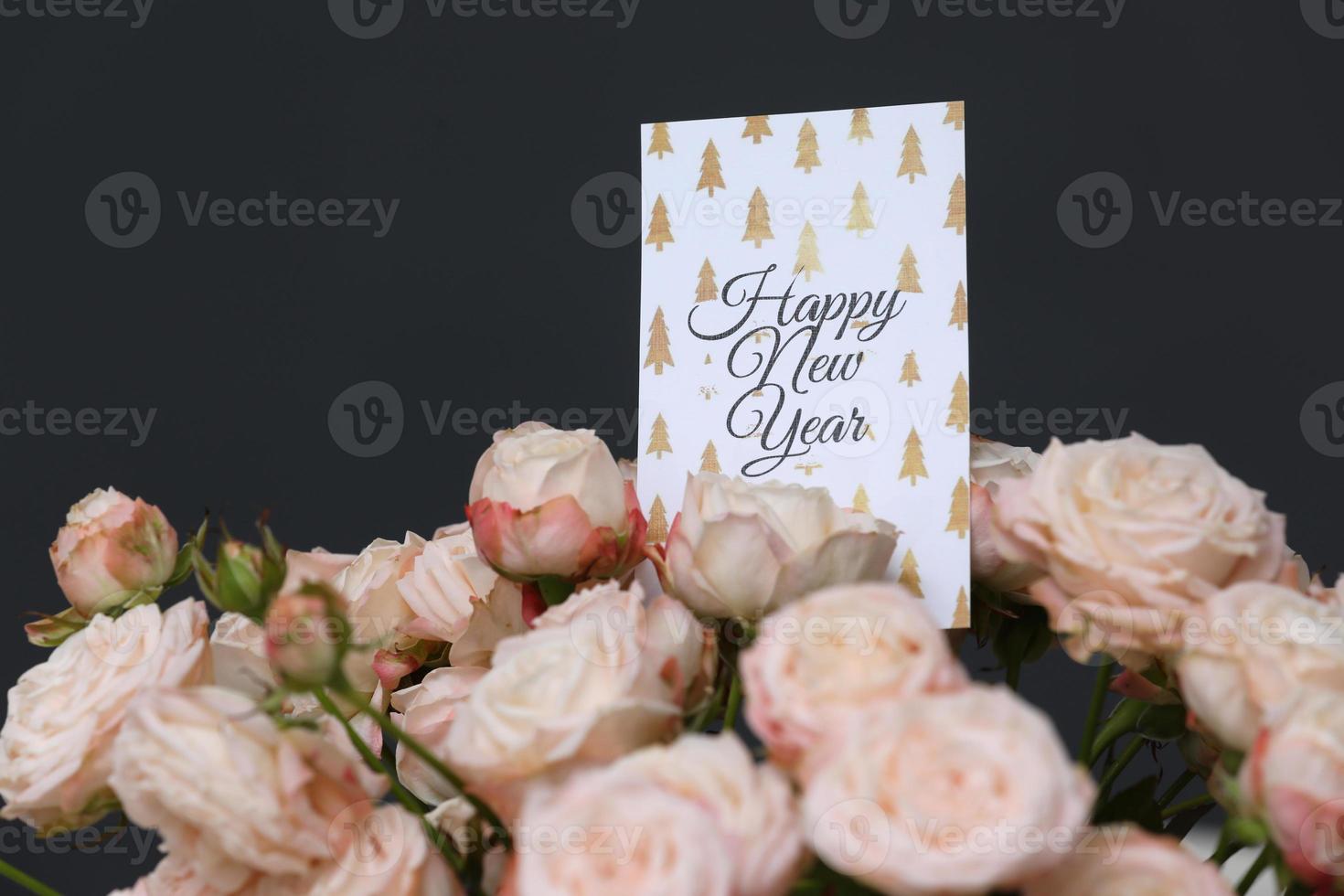 närbild vackra färska rosa rosor blommor med gott nytt år gratulationskort på grå bakgrund. kopieringsutrymme. foto