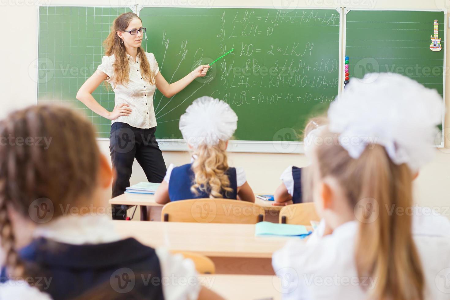 lärare nära tavlan som undervisar barn matematik eller geometri, håller pekaren. foto