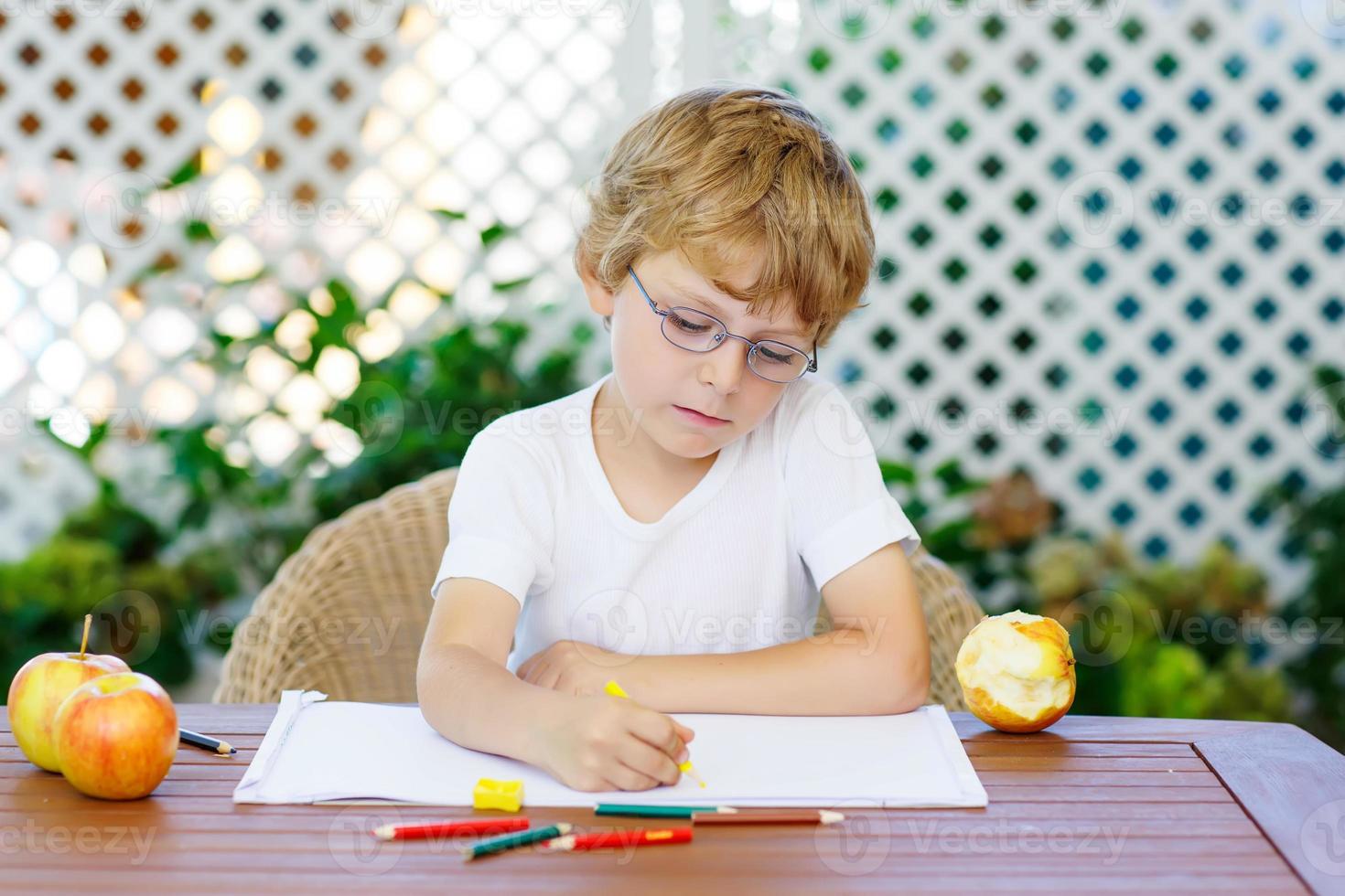 liten pojke med glasögon som gör läxor hemma foto