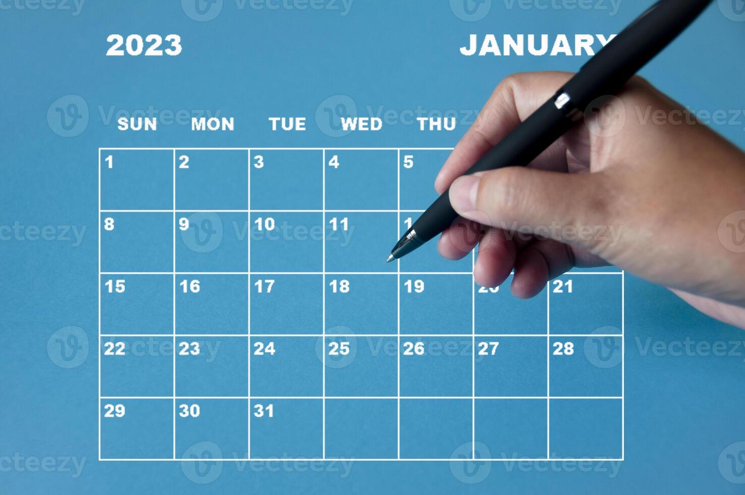 januari 2023 kalender med hand som håller svart penna på blå bakgrund. foto