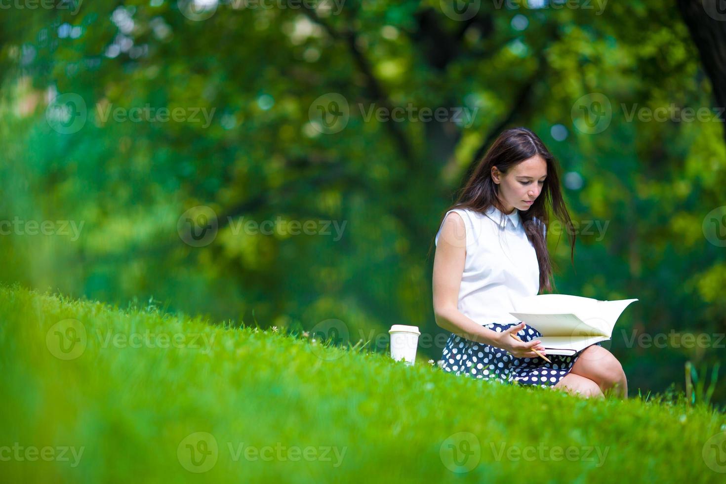 ung kvinna kopplar av med kaffe i parken som läser en bok foto