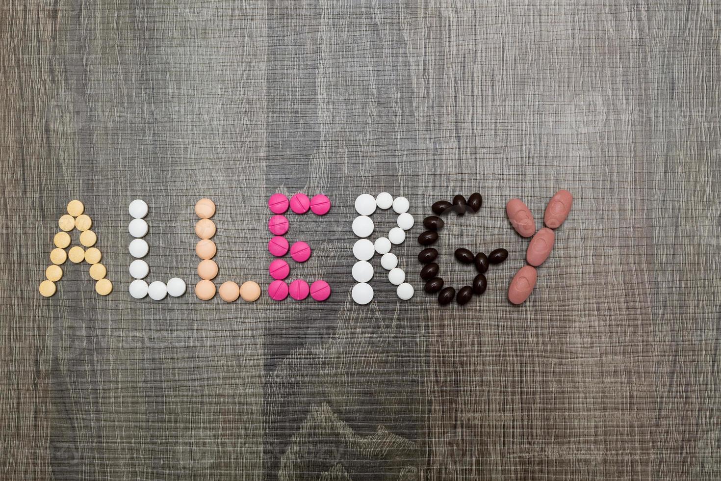 ordet allergi skrivet med piller på en träbakgrund. foto