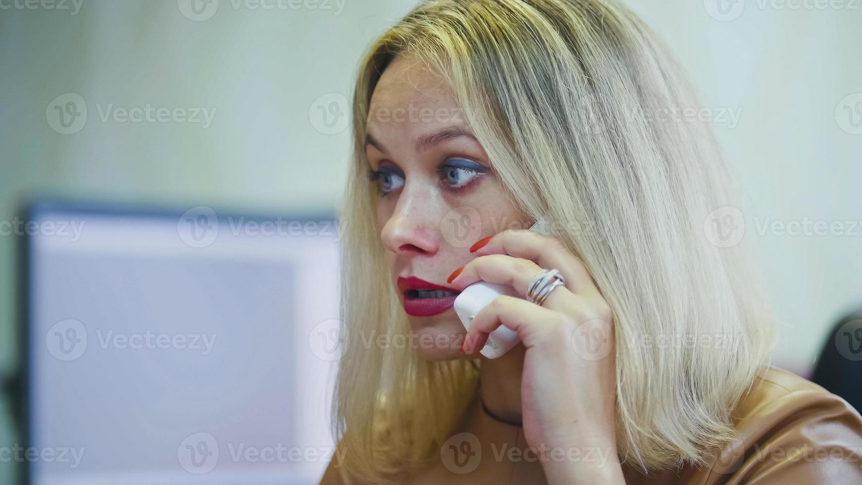 ung blond kvinna på kontoret pratar i telefon - framför datorn, handenhet med tråd närbild foto