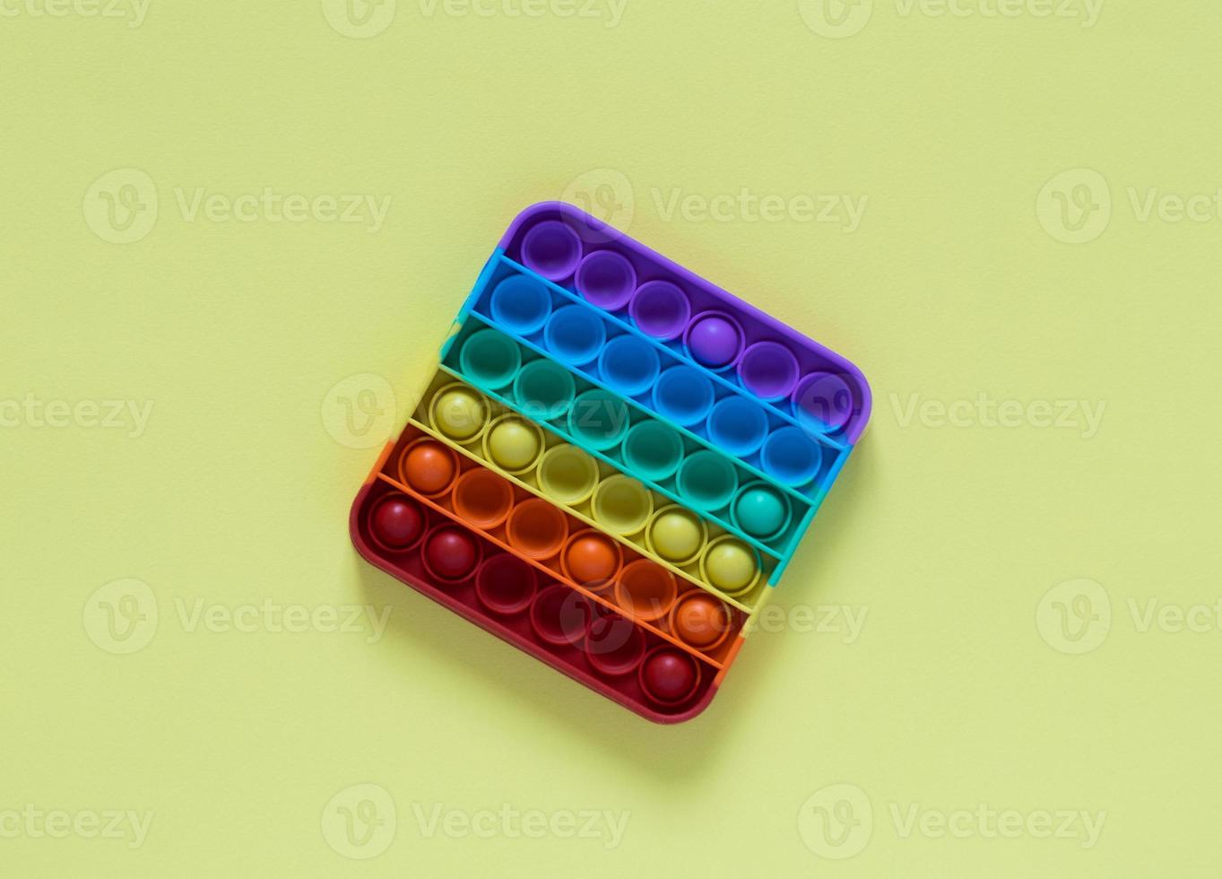 färgad leksak antistress för barn pop it. kvadrat med regnbågens färger isolerad på gul bakgrund. foto