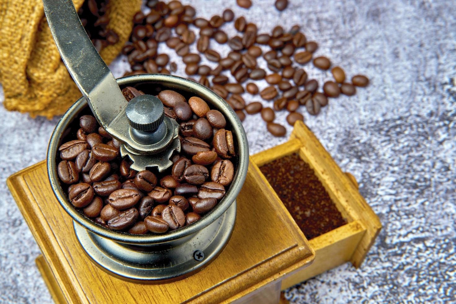 rostade kaffebönor i en antik handvev kaffekvarn. gammal retro handdriven kaffekvarn av trä och metall. mjukt fokus. foto