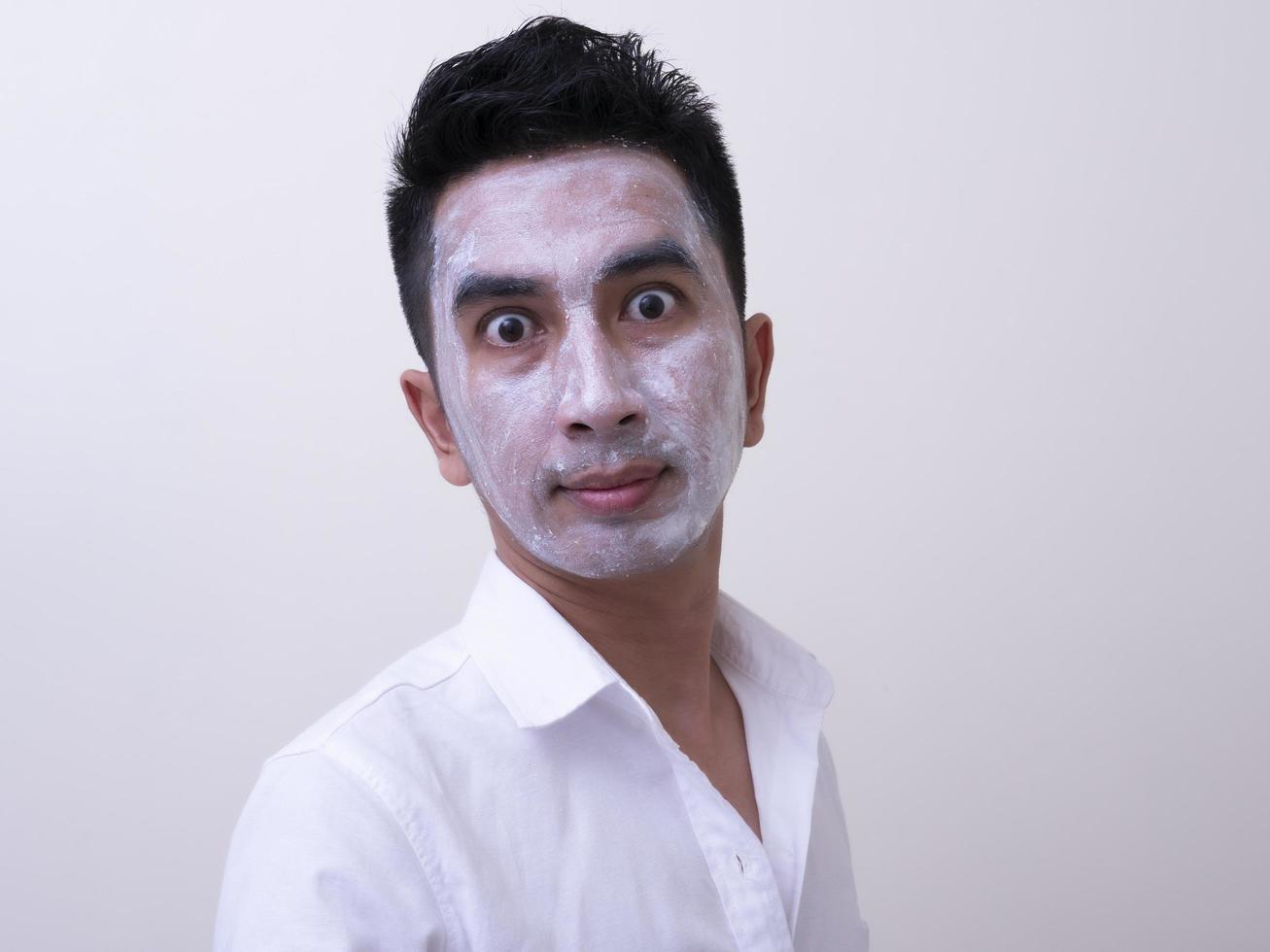 asiatisk stilig ung man applicerar grädde i ansiktet med smiley, hudvårdskoncept foto