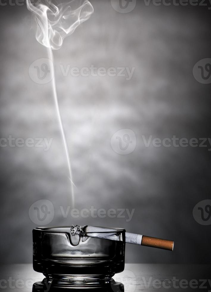brinnande cigarett i glas askfat foto