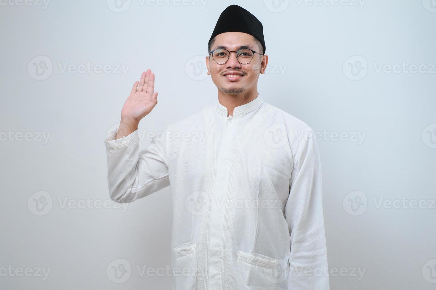 asiatisk muslimsk man som ler mot kameran medan viftar med handen säger hej foto