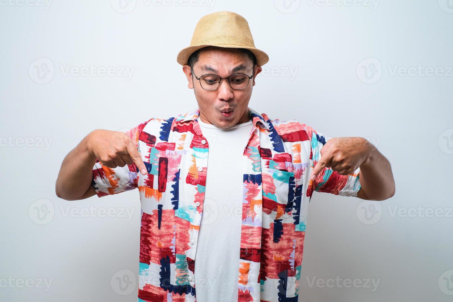 porträtt av glad asiatisk turist i ledig skjorta, bucket hat och trendiga solglasögon som står och pekar något med fingret över vit bakgrund. foto