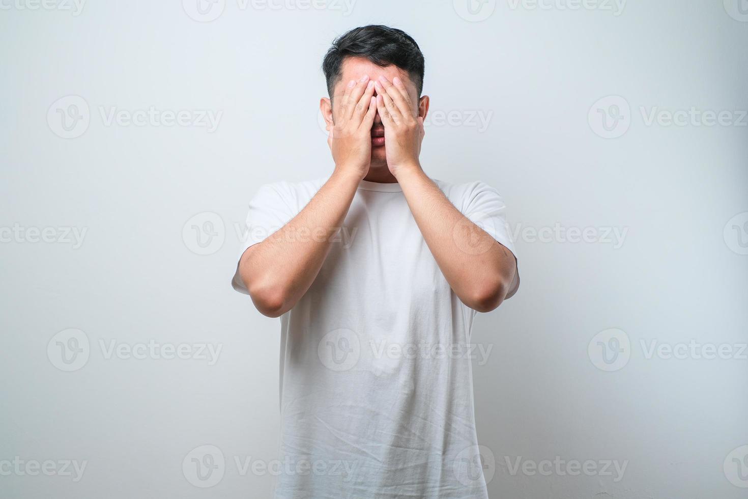 ung stilig asiatisk man bär avslappnad skjorta och glasögon med sorgligt uttryck som täcker ansikte med händer medan han gråter. depression koncept foto
