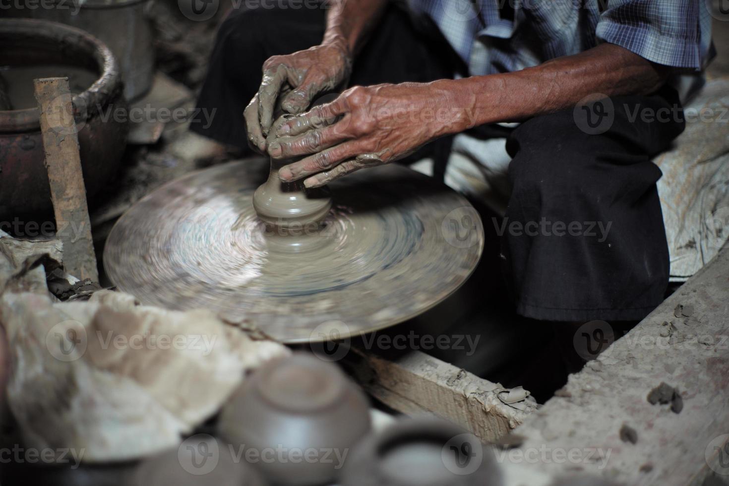 selektivt fokuserat på den smutsiga skrynkliga huden, händerna på en gammal man som formar leran arbetar på snurrhjulet för att göra burken med suddig grupp av lerburkar i förgrunden foto