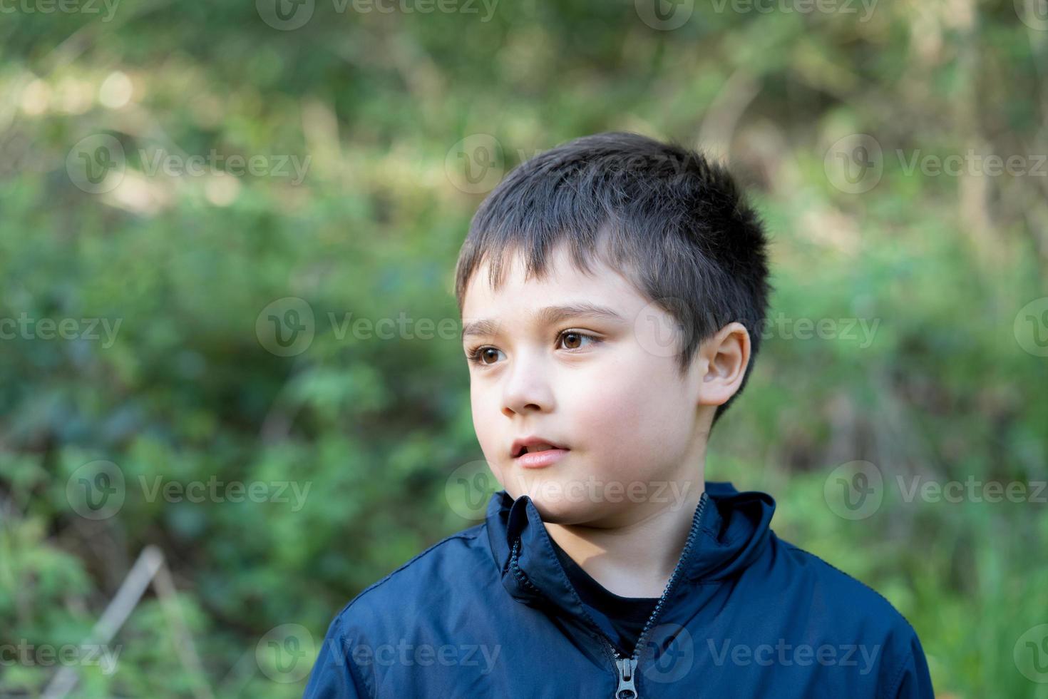 glad ung pojke som leker utomhus i trädgården, porträttbarn med leende ansikte tycker om att leka ute på morgonen, barn kopplar av en solig dag på våren eller sommaren i parken. foto