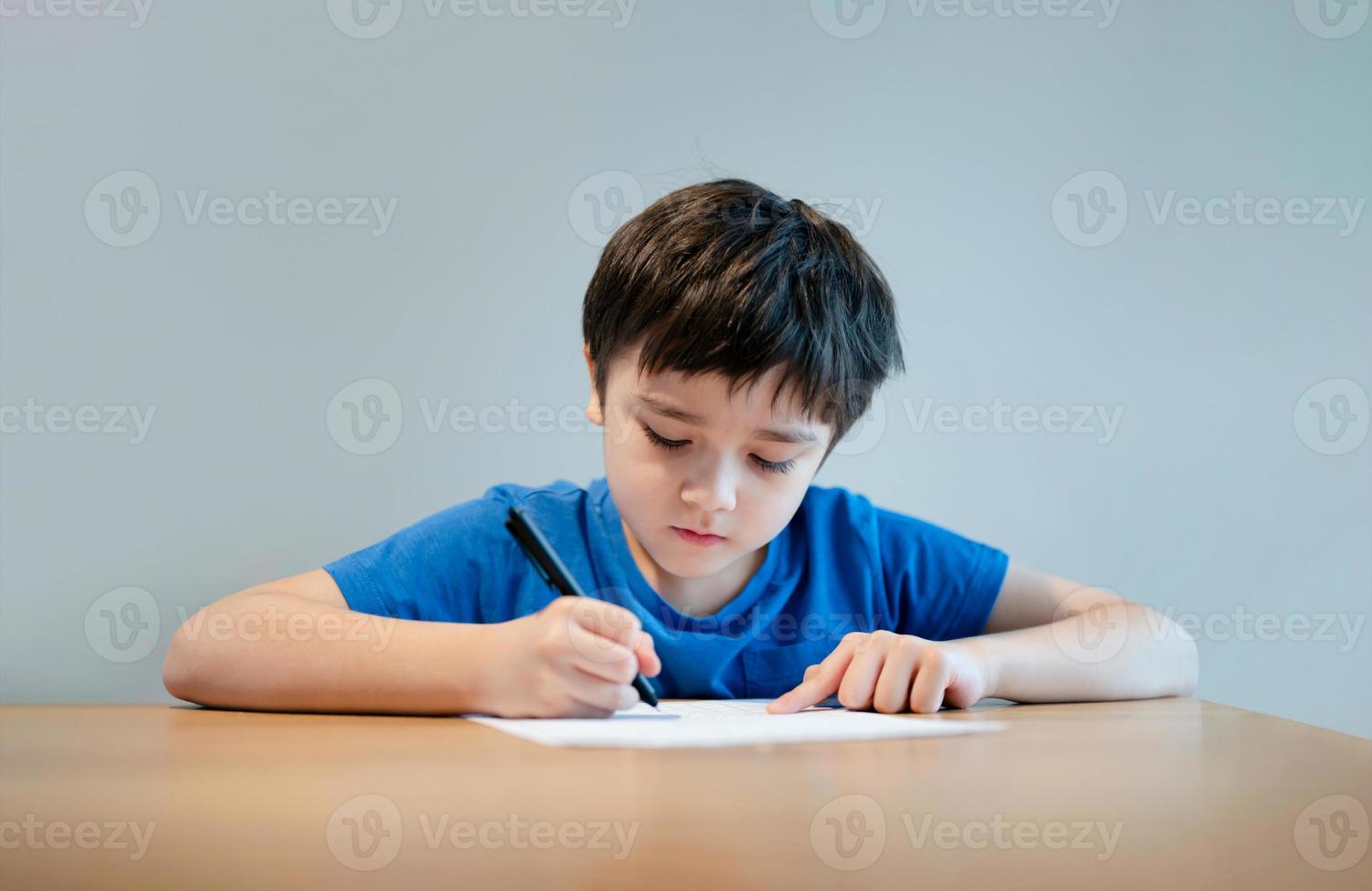 skolbarn som använder svart pennteckning eller skriver brevet på papper, ung pojke gör läxor, barn med penna skriver anteckningar i pappersark under lektionen. söt elev gör test, hemundervisningskoncept foto