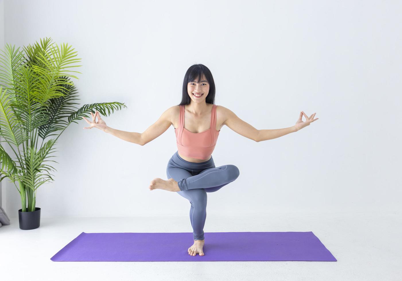 asiatisk kvinna som utövar yoga inomhus med förväg balanserande position för att kontrollera andningen i enbensställning foto