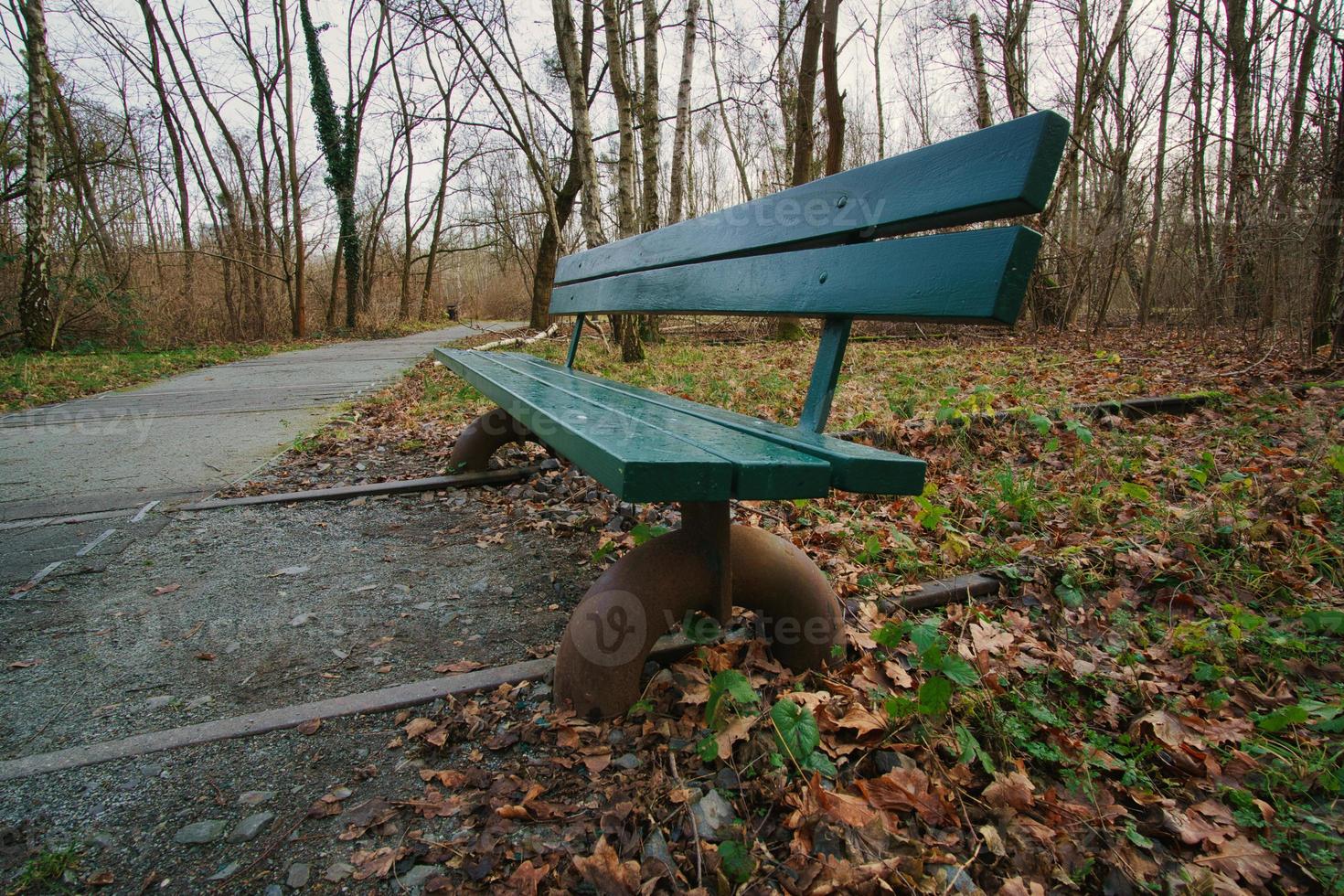 trä parkbänk över övergivna järnvägsspår i en park på hösten. ensam njuta foto