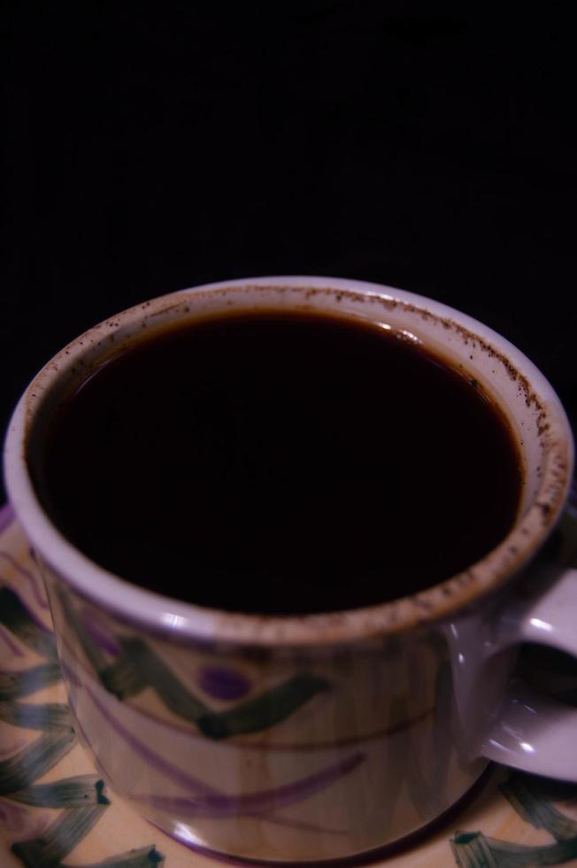 ett glas innehållande bryggt svart kaffe på svart bakgrund foto