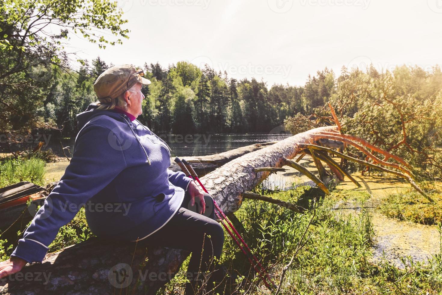 äldre kvinna sitter på trädgren på sjöstranden njuta av sommardag utomhus. textur och natur välbefinnande koncept bakgrund foto