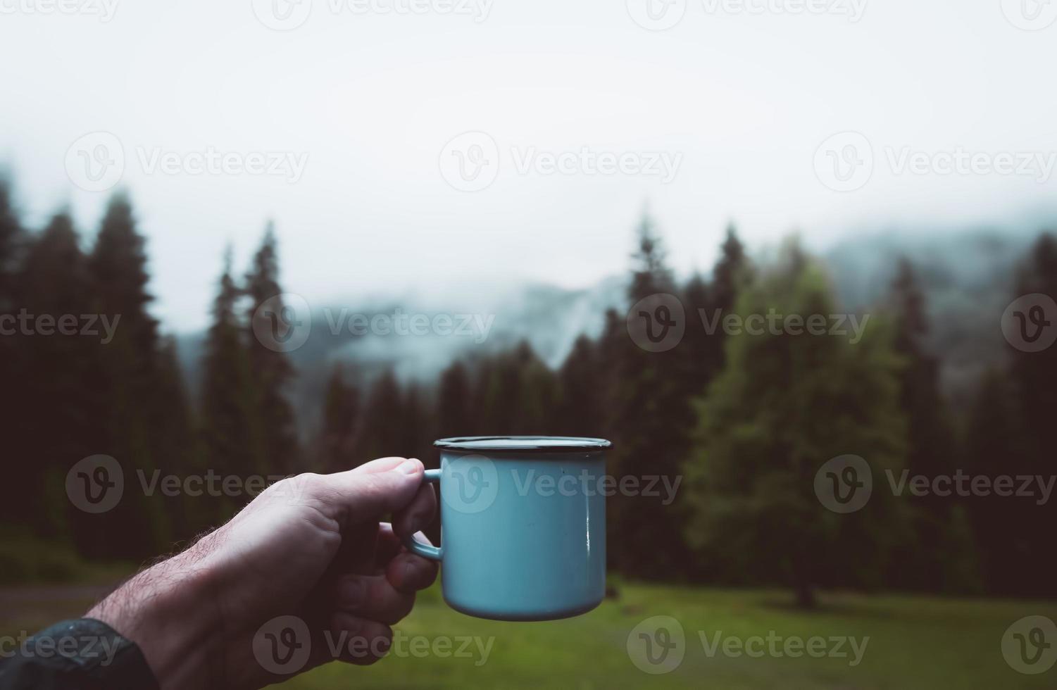blå kopp i händer med skog bakgrund. filmisk resa inspirerande bakgrund foto