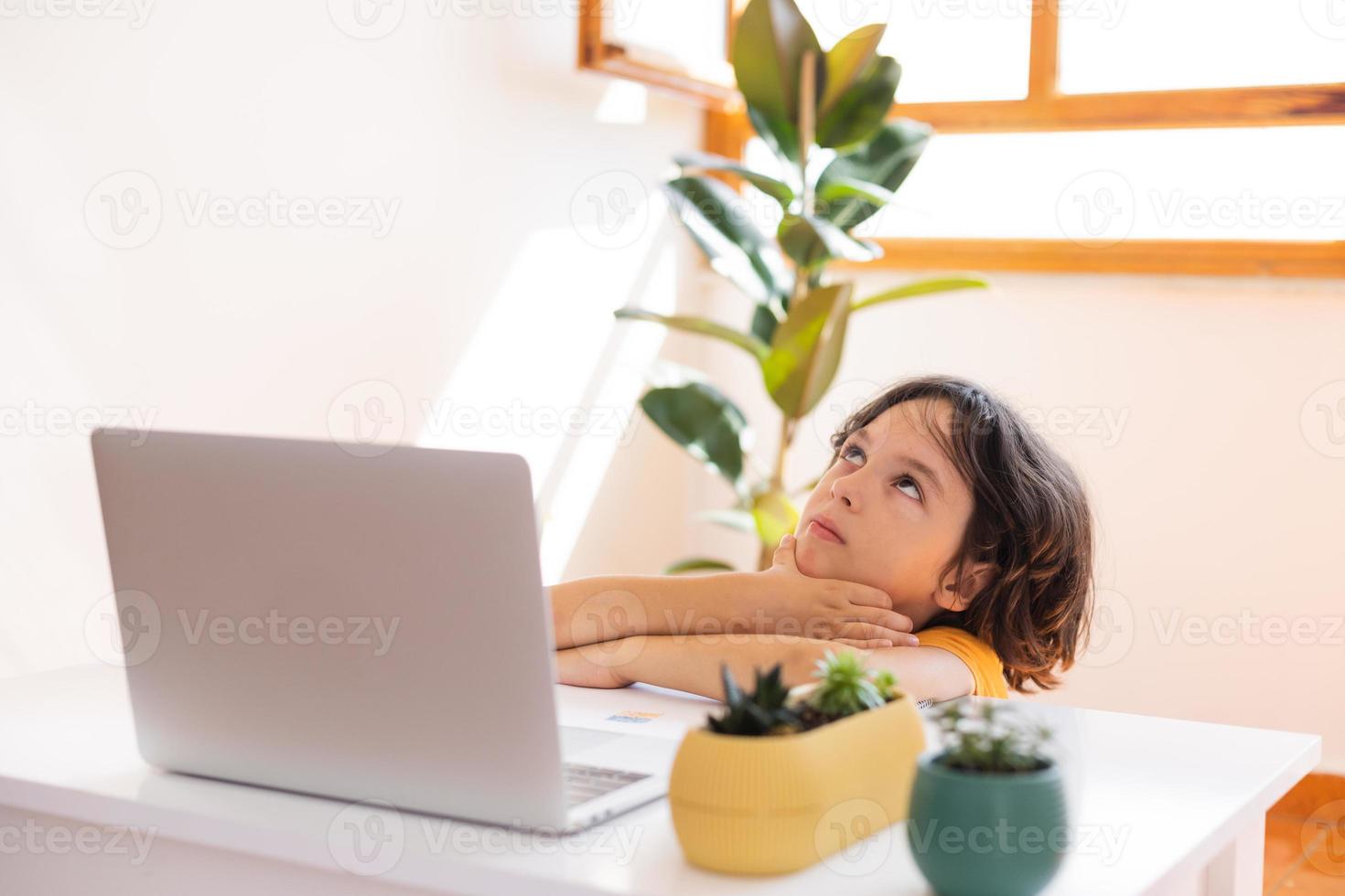 porträtt av en uttråkad pojke, barnpojke använder en bärbar dator och studerar online foto